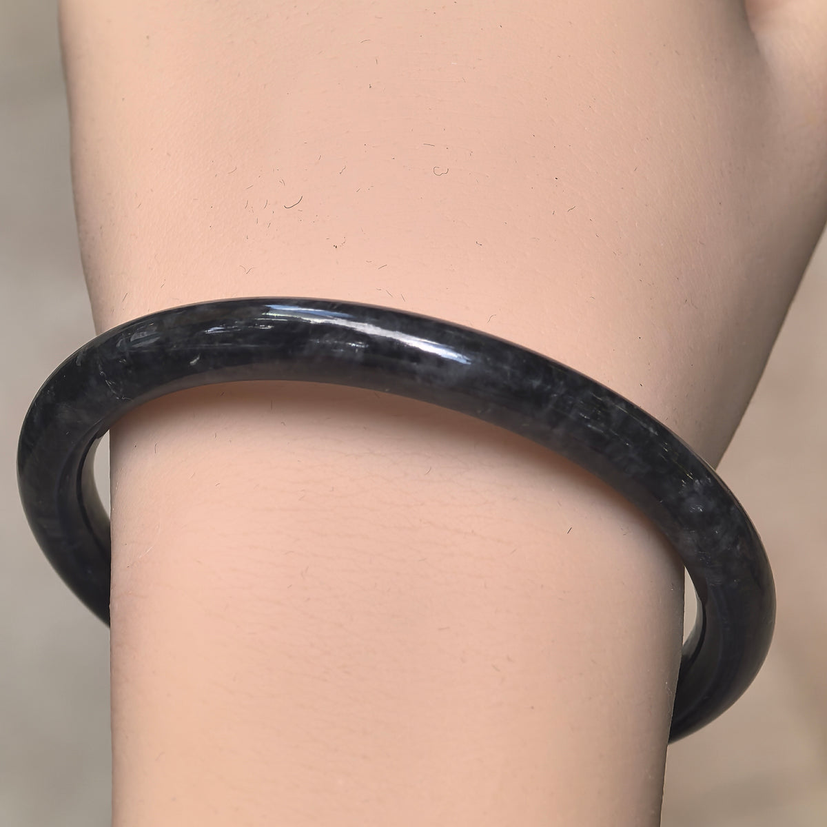 Front wrist view of a dark jadeite bangle showing subtle gray mottling and its slender rounded shape.
