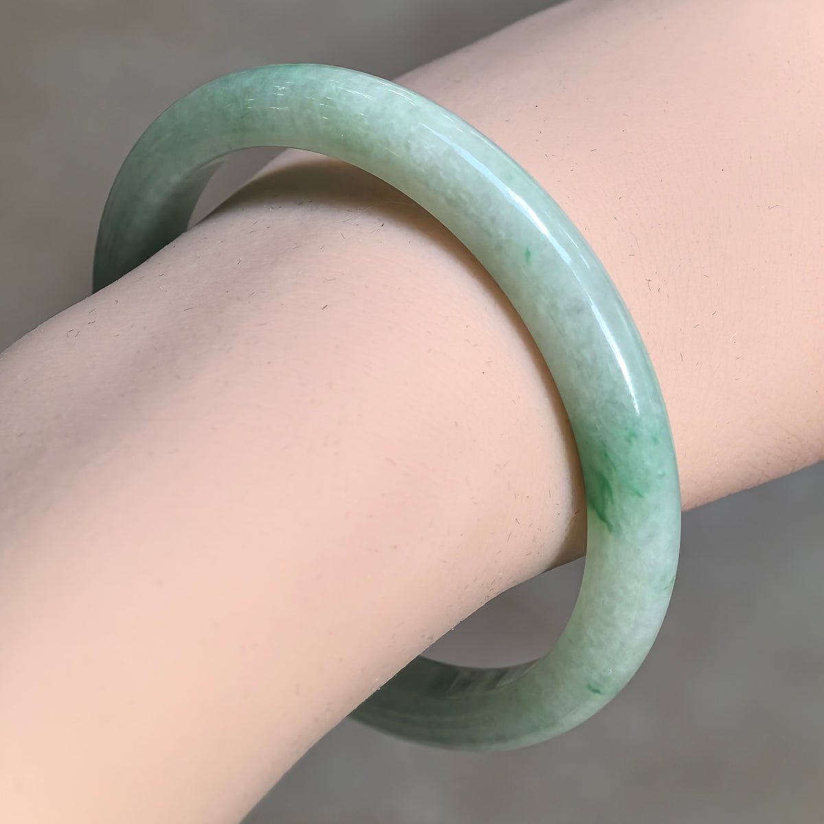 Angled wrist view of a green jadeite bangle showing its polished curved exterior and concentrated green patches.