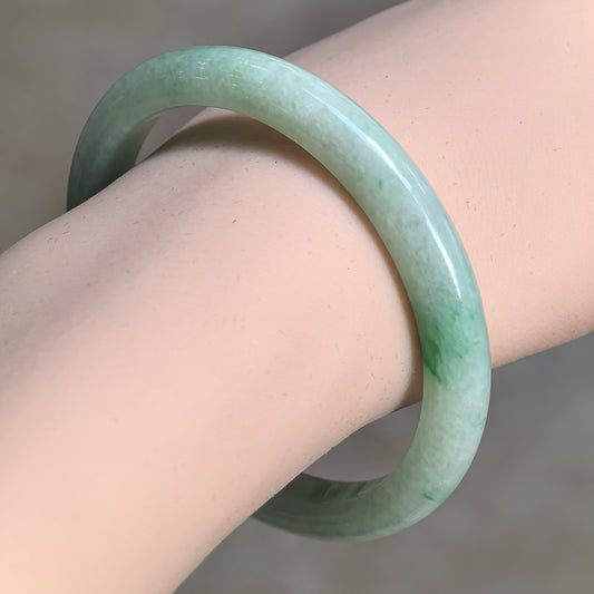 Angled wrist view of a green jadeite bangle showing its polished curved exterior and concentrated green patches.
