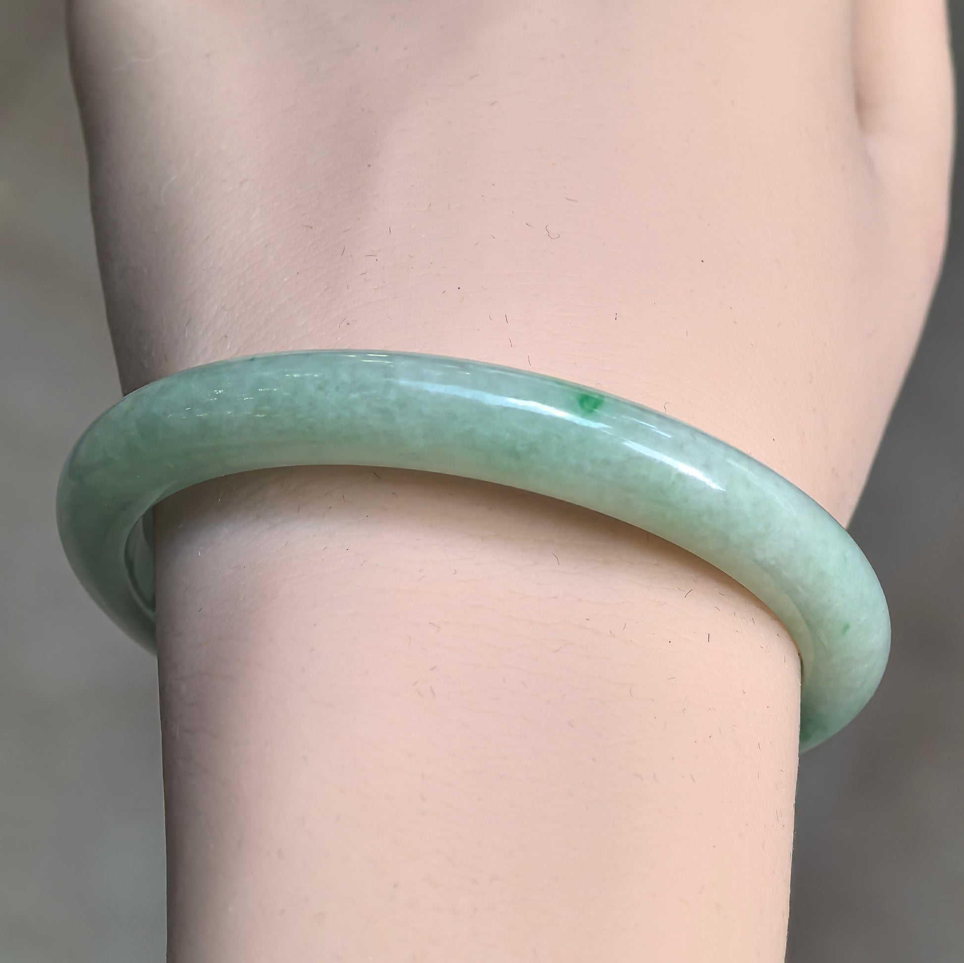 Front wrist view of an apple green jadeite bangle with a slim D-shape profile and small deeper green accents.