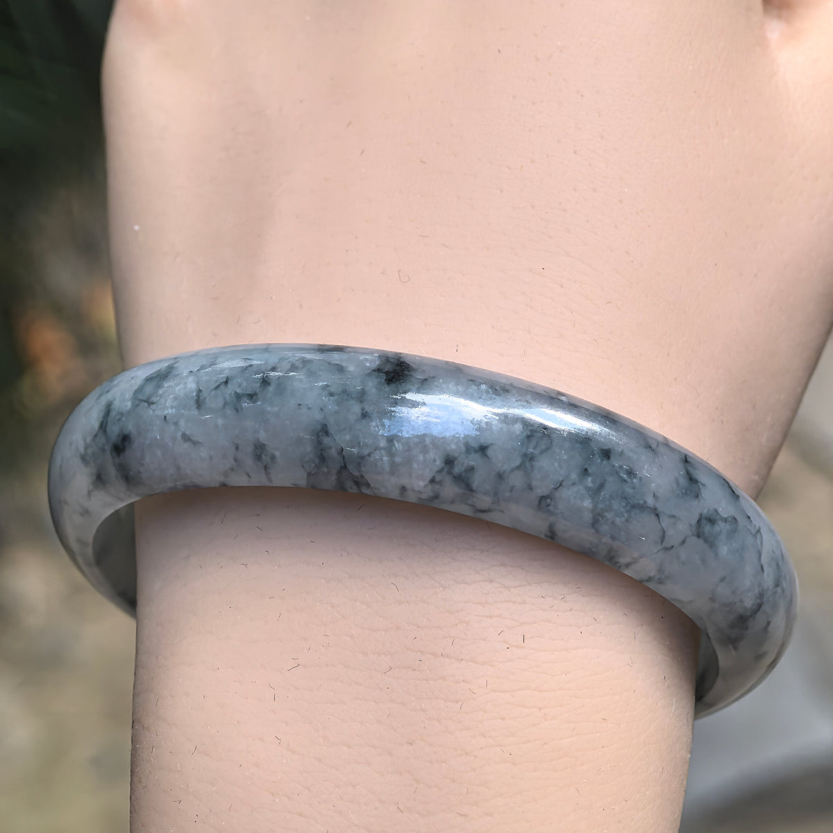 Front wrist view of a polished oval jadeite bangle showing fine branching blue patterns across the broad outer face.