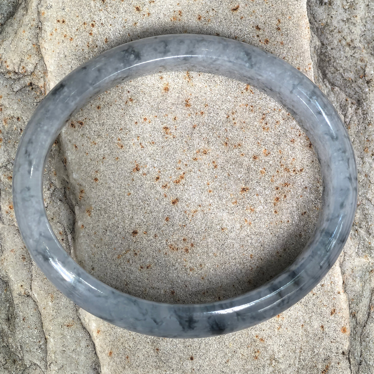 Top view of an oval jadeite bangle on pale stone, showing the elongated opening and natural blue patterns around the band.