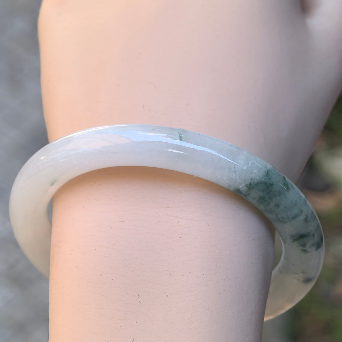 Front wrist view of a white and light green jadeite bangle showing concentrated green patterns along one side of its rounded band.