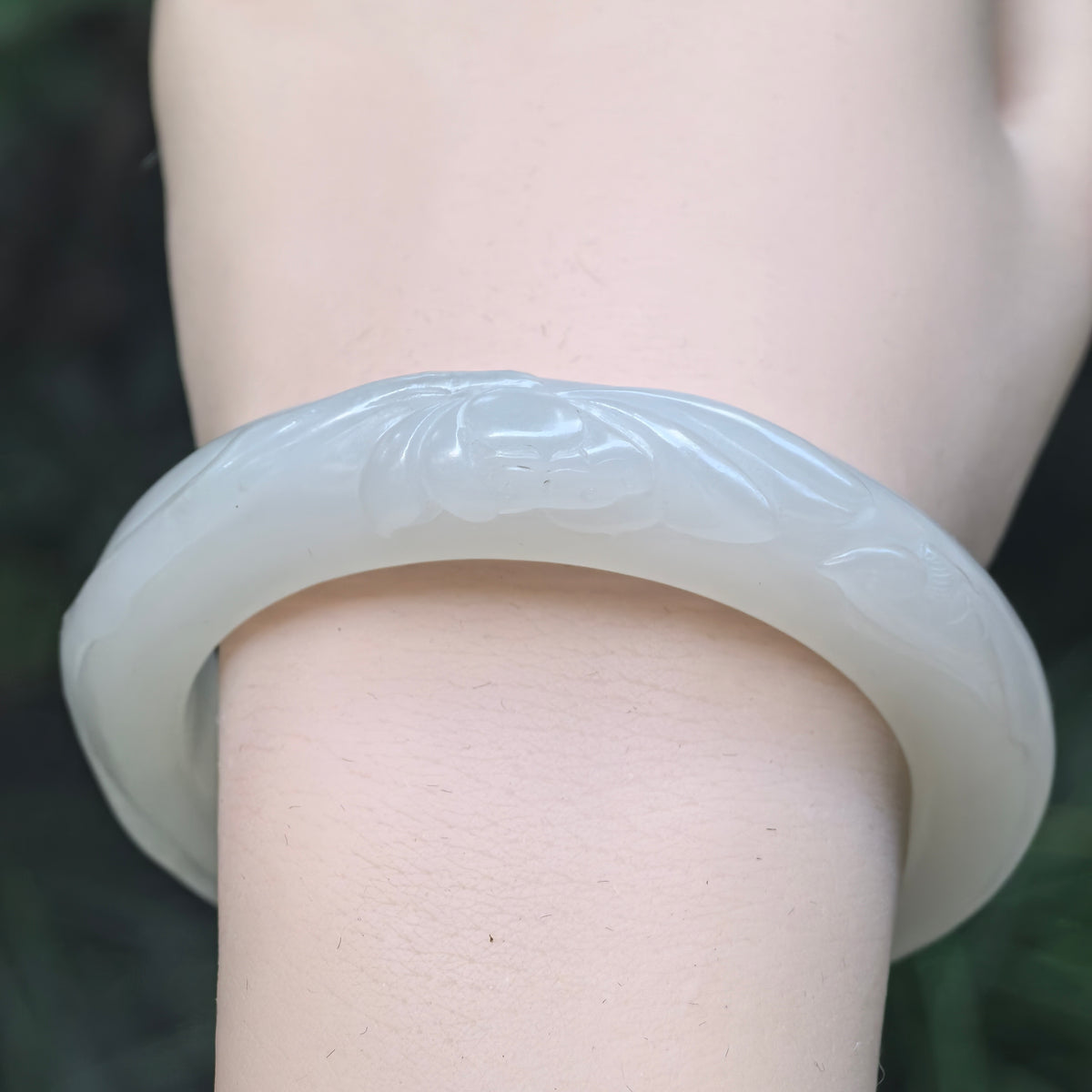 Front wrist view of a white Hetian jade D-shape bangle, with the lotus carving centered across the visible outer band.