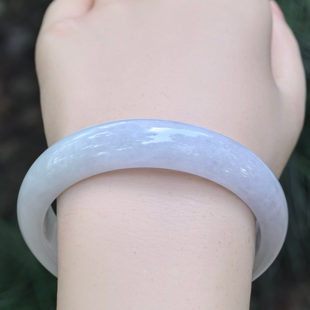 Front wrist view of a white glutinous jadeite bangle showing its broad band and softly clouded texture.