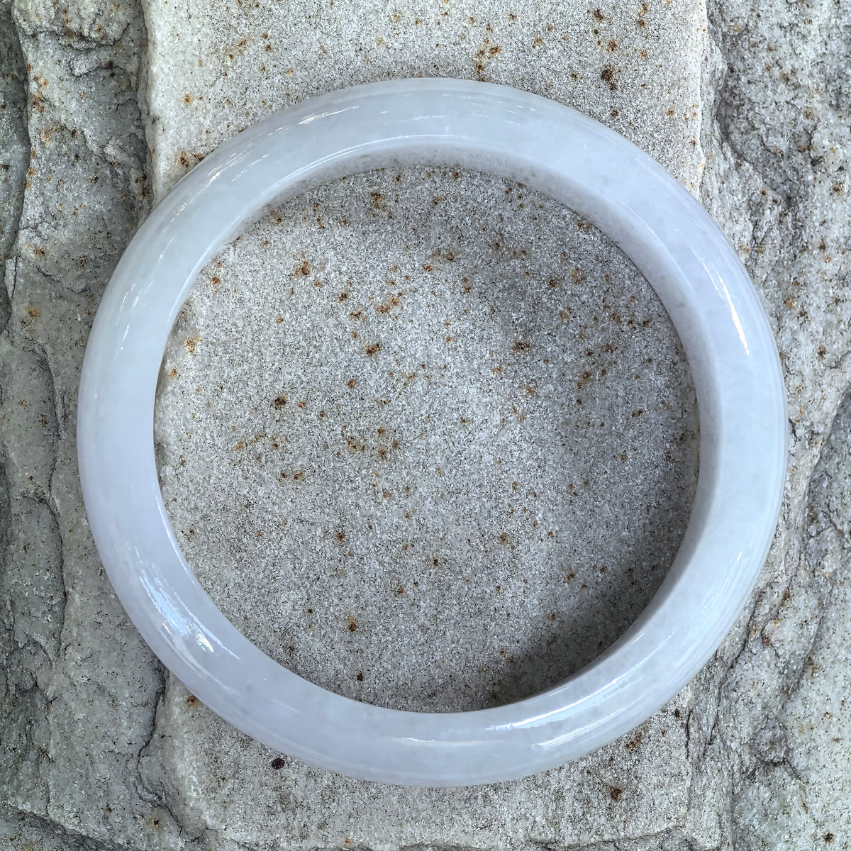 Top view of a white jadeite bangle on pale stone, showing its circular outline and subtle internal clouding.