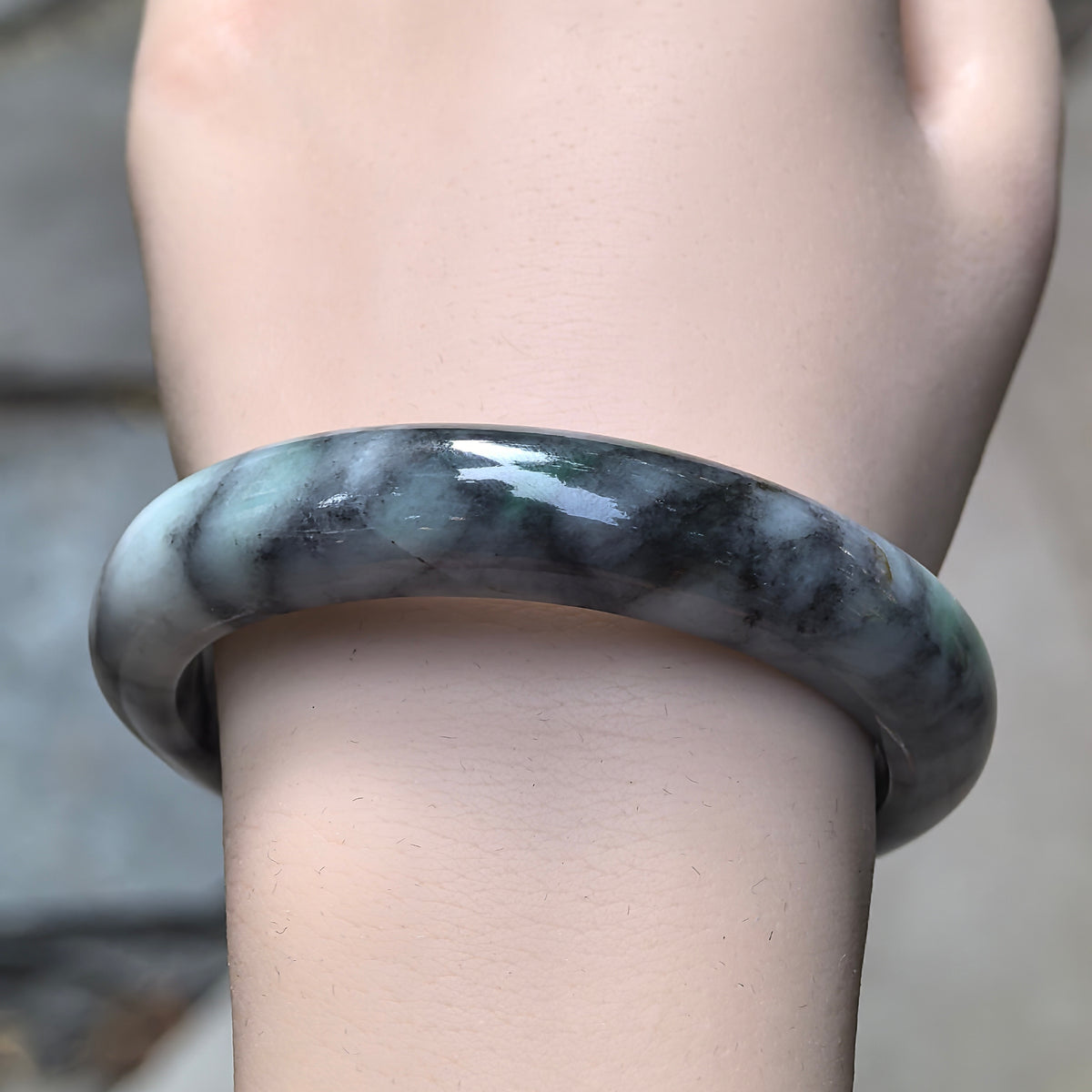 Front wrist view of a gray and black D-shape jadeite bangle with contrasting pale patches and a polished outer face.