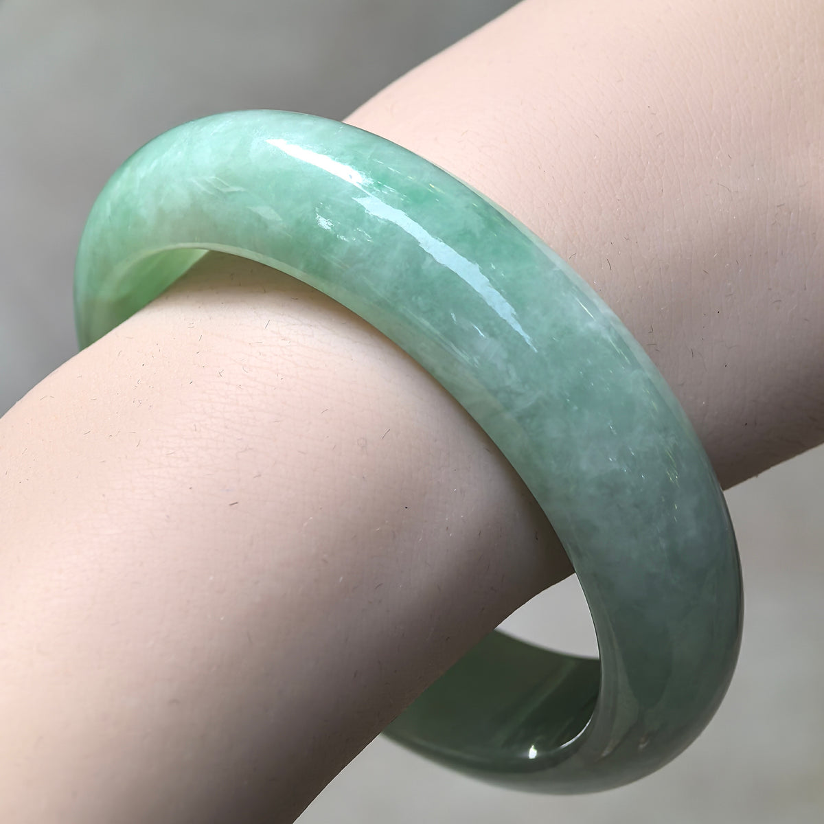 Angled wrist view of an apple green jadeite bangle with a rounded outer face and lighter natural color variations.