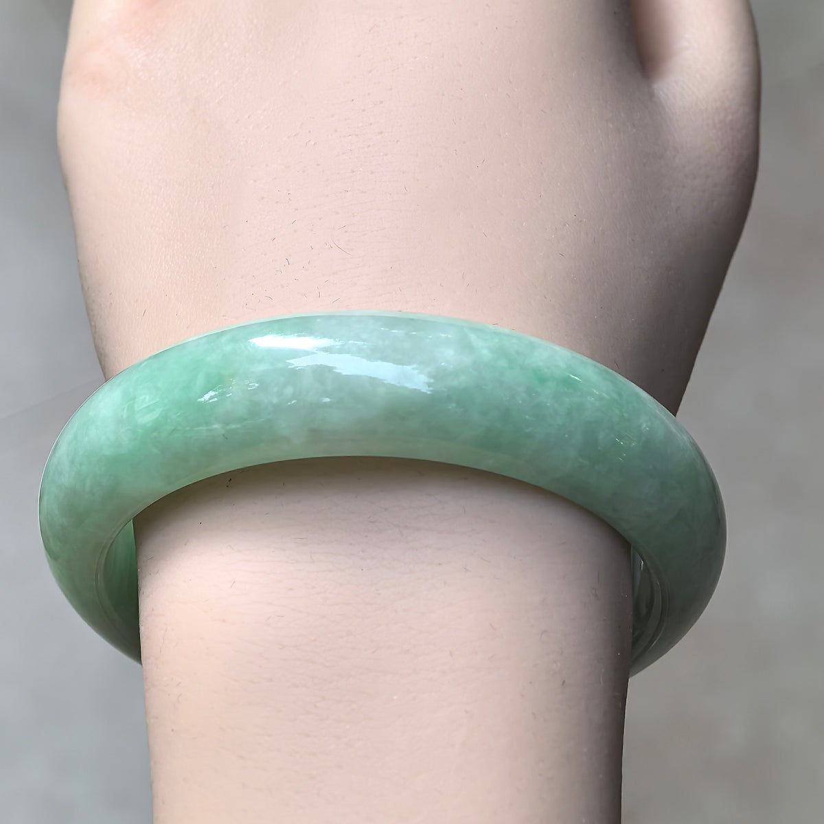 Front wrist view of an apple green D-shape jadeite bangle showing its broad polished band and softly cloudy texture.