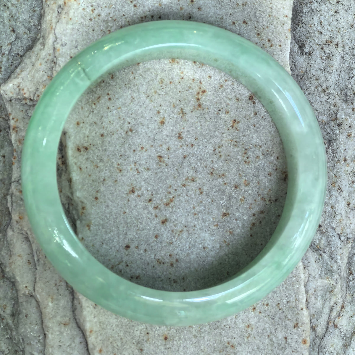 Top view of an apple green jadeite bangle on pale stone, with a visible stained crack near the upper left side.