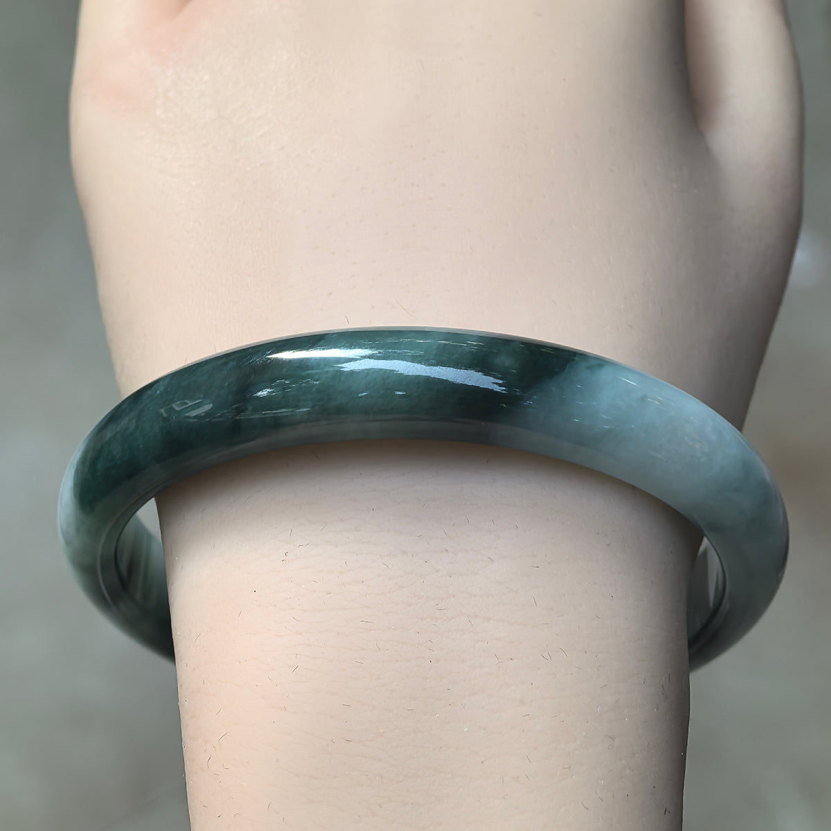 Front wrist view of a green glutinous jadeite bangle showing a broad dark green section blending into a lighter green area.