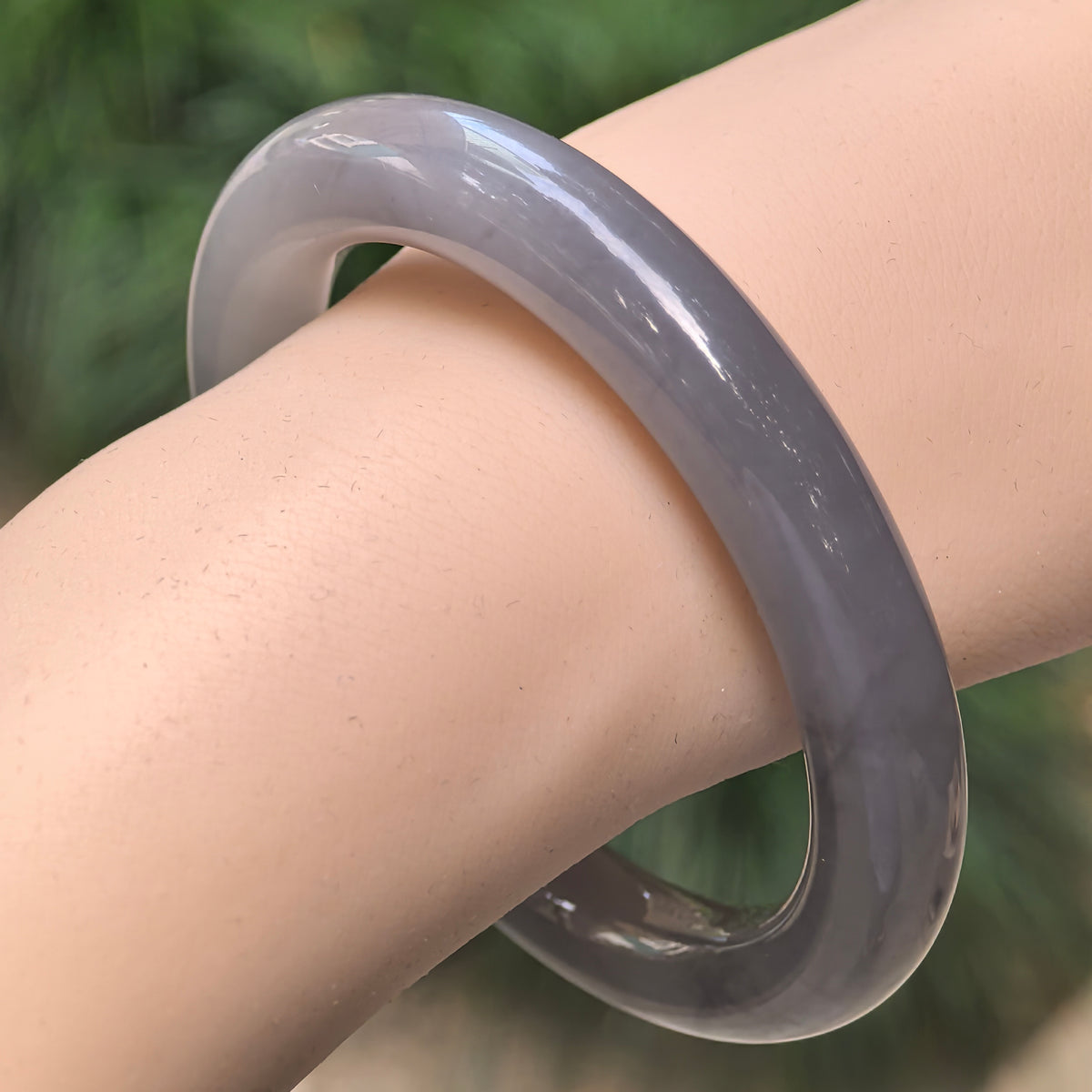 Angled wrist view of a smoky purple Hetian jade round-bar bangle showing its rounded inner surface and subtle tonal variations.