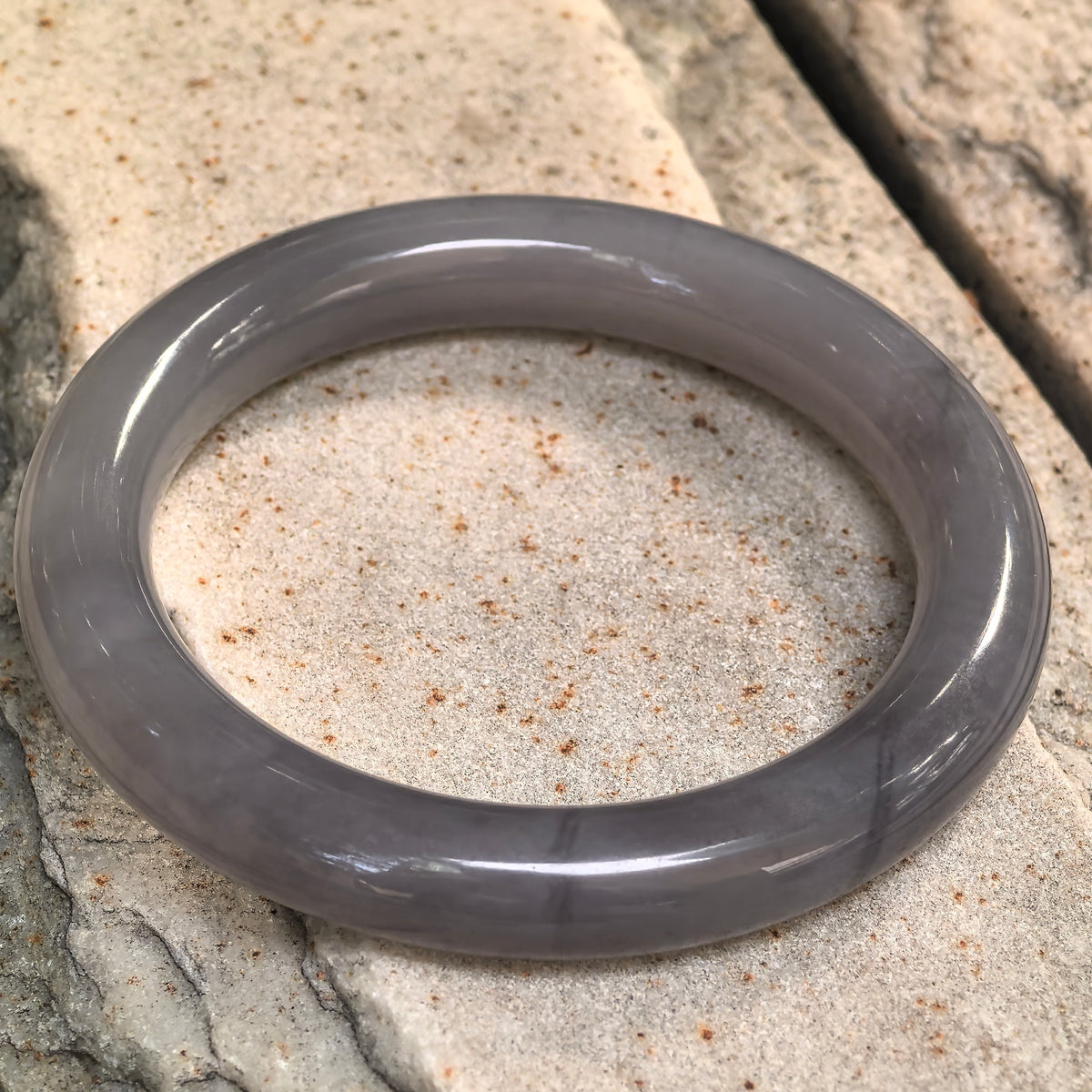Smoky purple nephrite bangle resting at an angle on stone, with natural water lines visible along the front section.