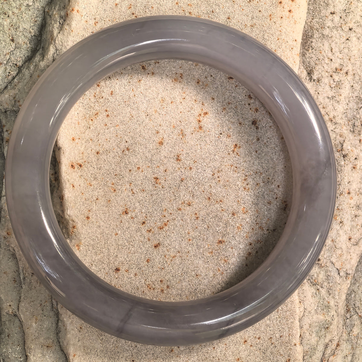 Top view of a smoky purple round-bar Hetian jade bangle on stone, showing its circular outline and polished surface.