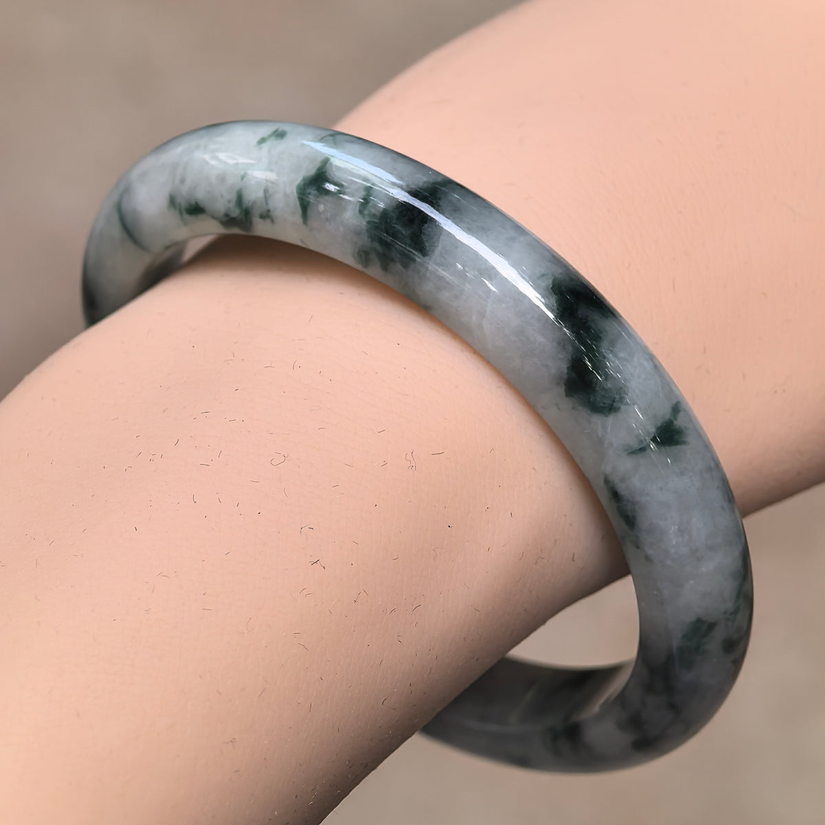 Angled wrist view of a D-shape jadeite bangle with deep green floating patterns contrasting against a milky pale base.