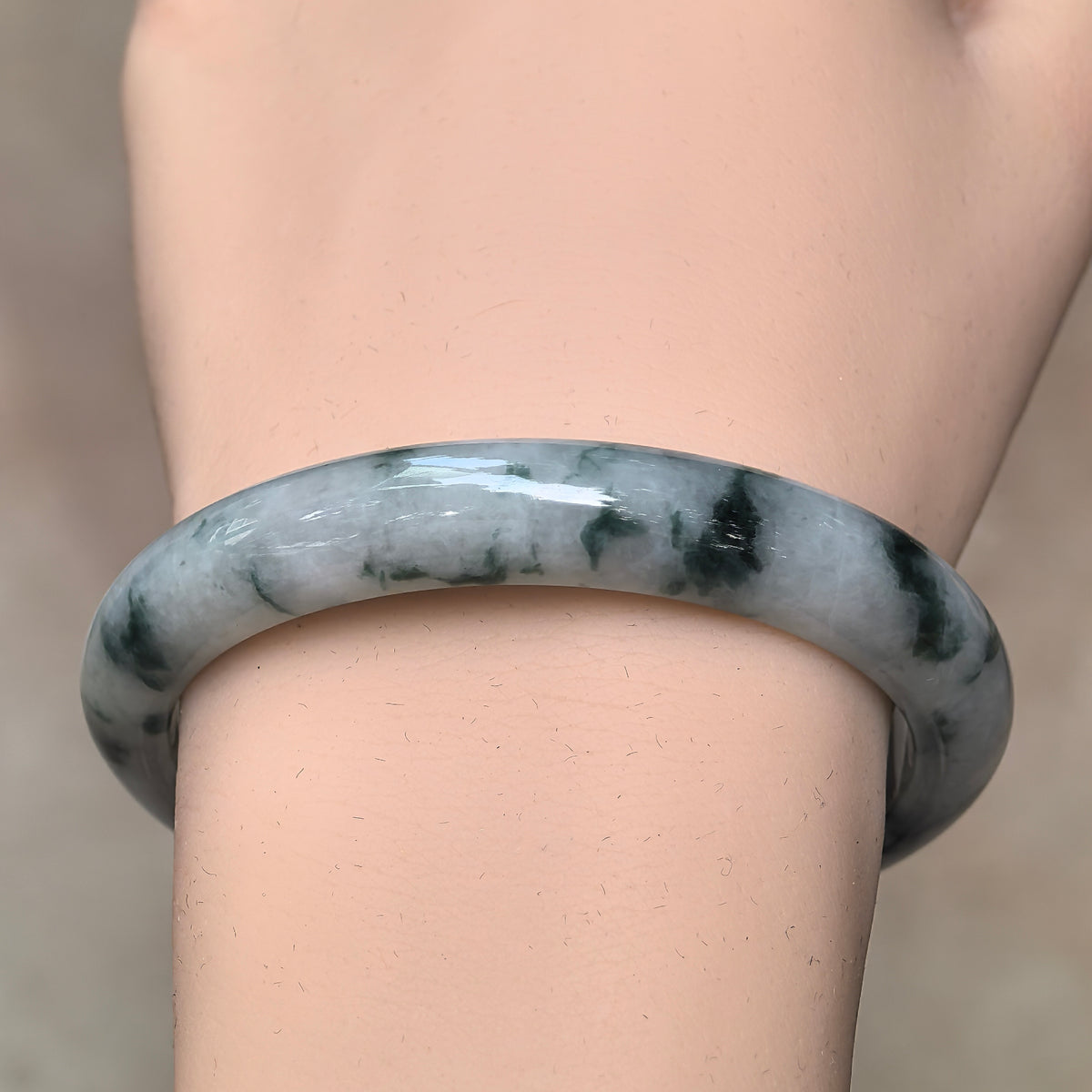 Front wrist view of a glutinous jadeite bangle showing scattered green wisps, darker patches, and a polished rounded exterior.