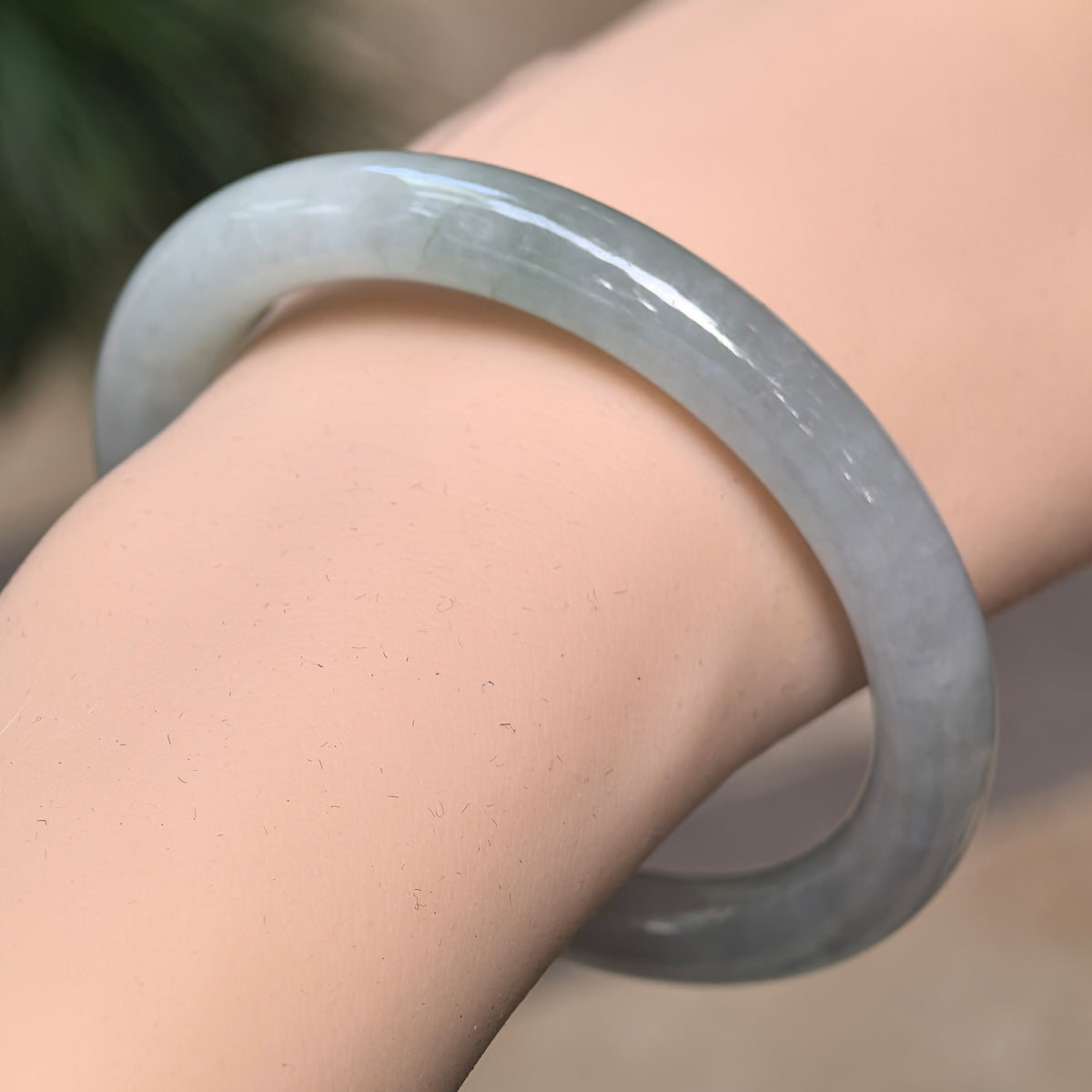 Angled wrist view of a light green round-bar jadeite bangle showing its polished curves and soft, cloudy texture.