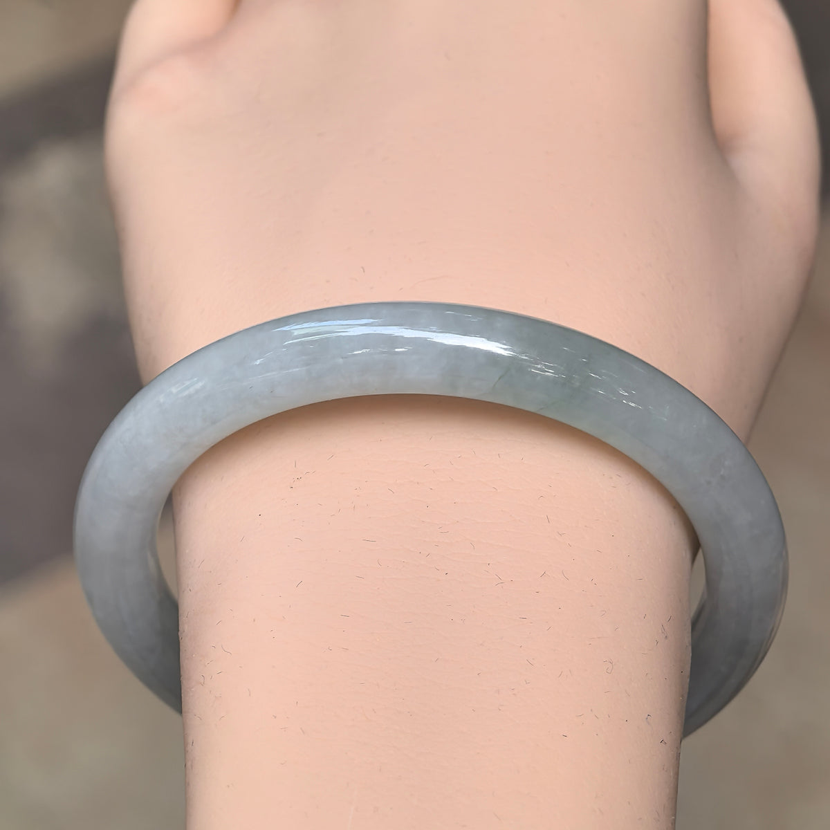 Front wrist view of a pale green jadeite bangle with a rounded band and a fine crack visible near the upper section.