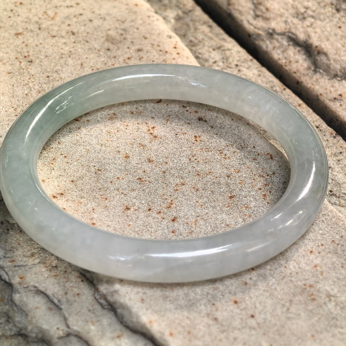 Light green round-bar jadeite bangle resting at an angle on stone, showing its rounded inner surface and subtle variations in color.