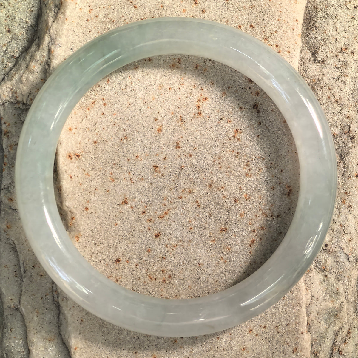 Top view of a fine glutinous light green jadeite bangle on stone, showing its circular outline and paler areas around the band.