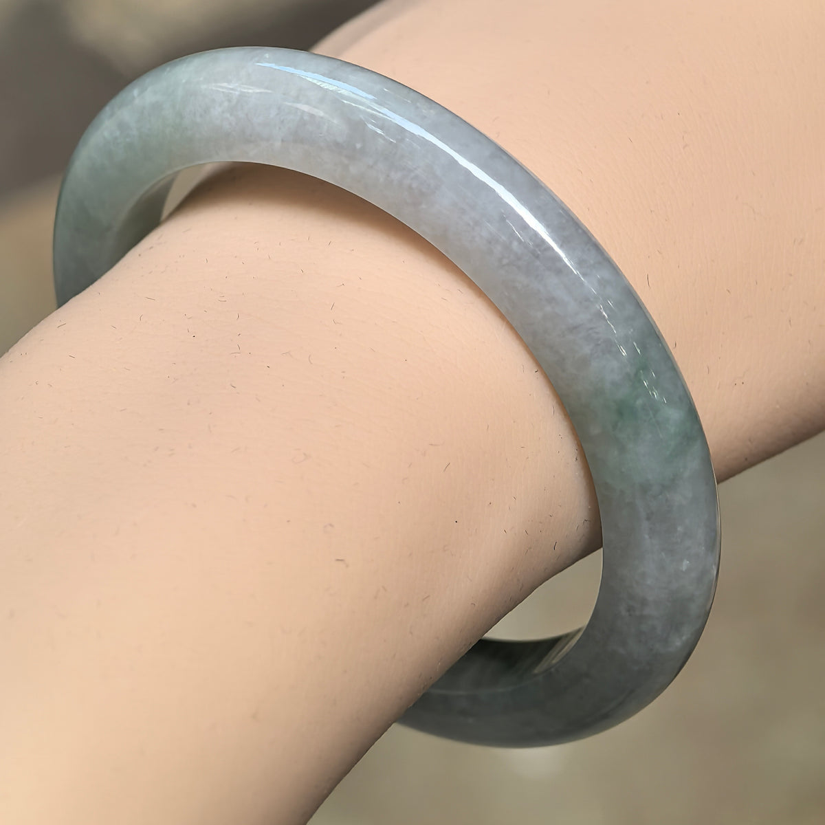 Angled wrist view of a light green D-shape jadeite bangle with darker green floating patterns and a polished surface.