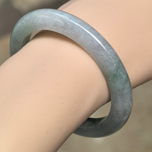 Angled wrist view of a light green D-shape jadeite bangle with darker green floating patterns and a polished surface.