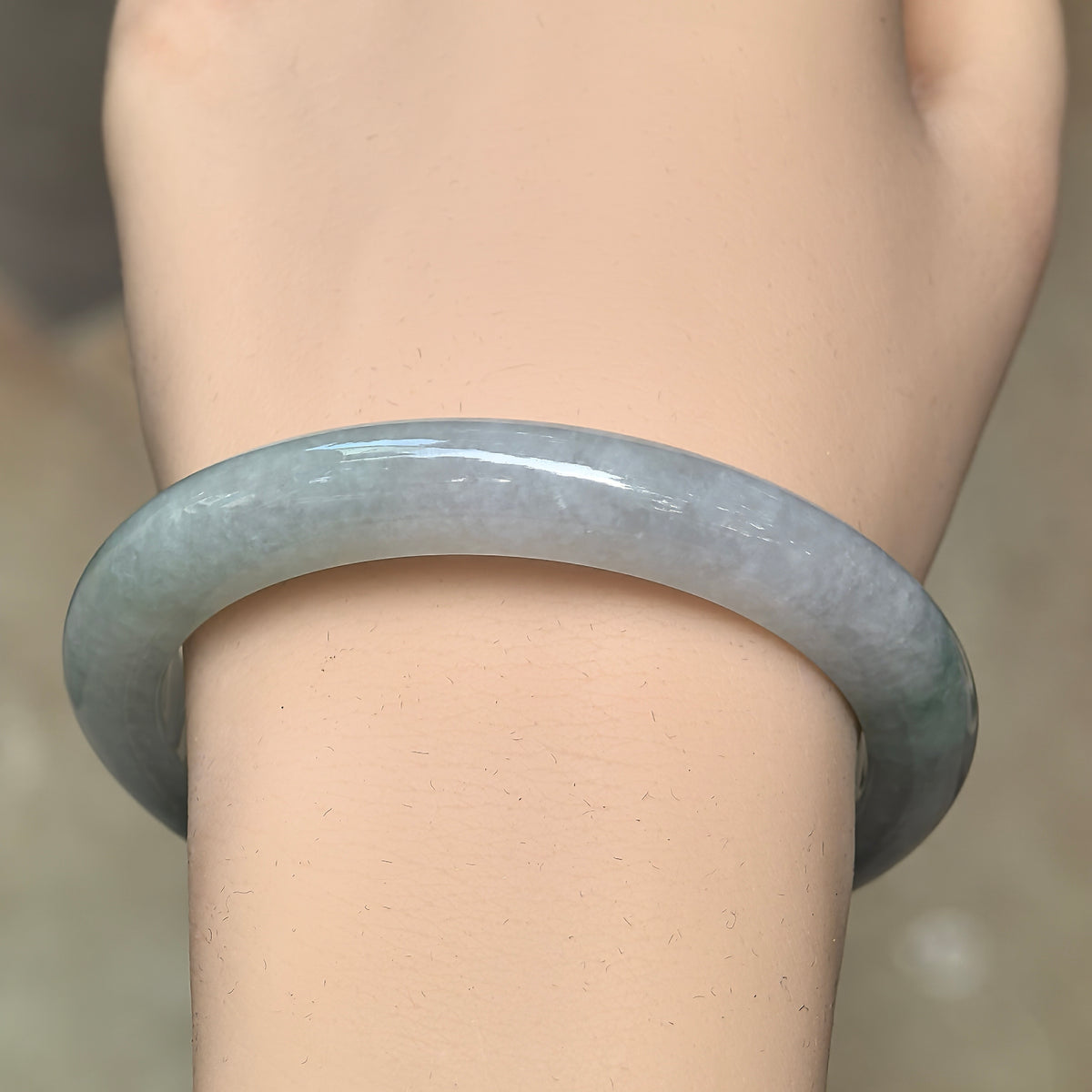 Front wrist view of a glutinous jadeite bangle showing its pale green base, softly cloudy texture, and deeper green accents.