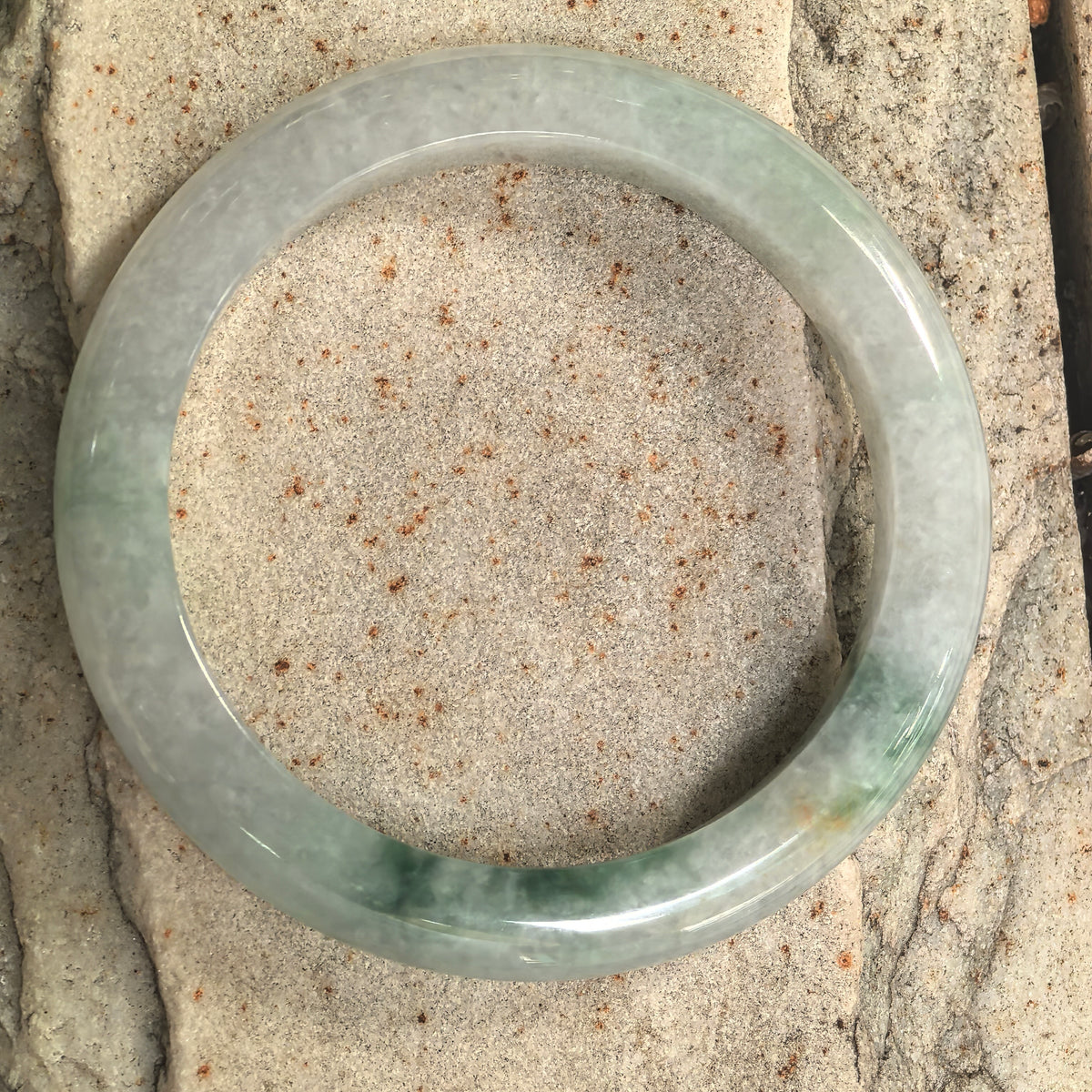 Top view of a D-shape jadeite bangle on stone, showing its circular outline and green floating patterns concentrated along the lower section.