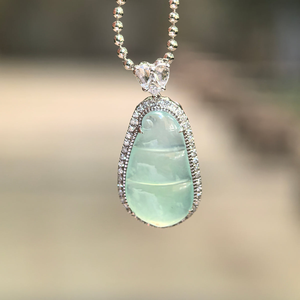 Light green jadeite bean pod pendant suspended from a beaded chain, showing its translucent carving, diamond border and decorative bail.