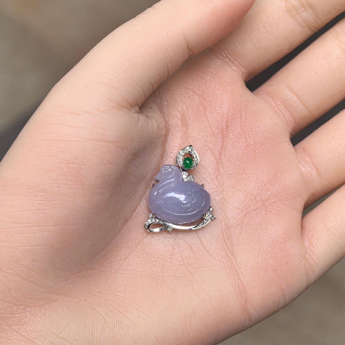 Lavender jadeite swan pendant displayed on an open palm, showing its proportions and decorative 18K gold and diamond setting.