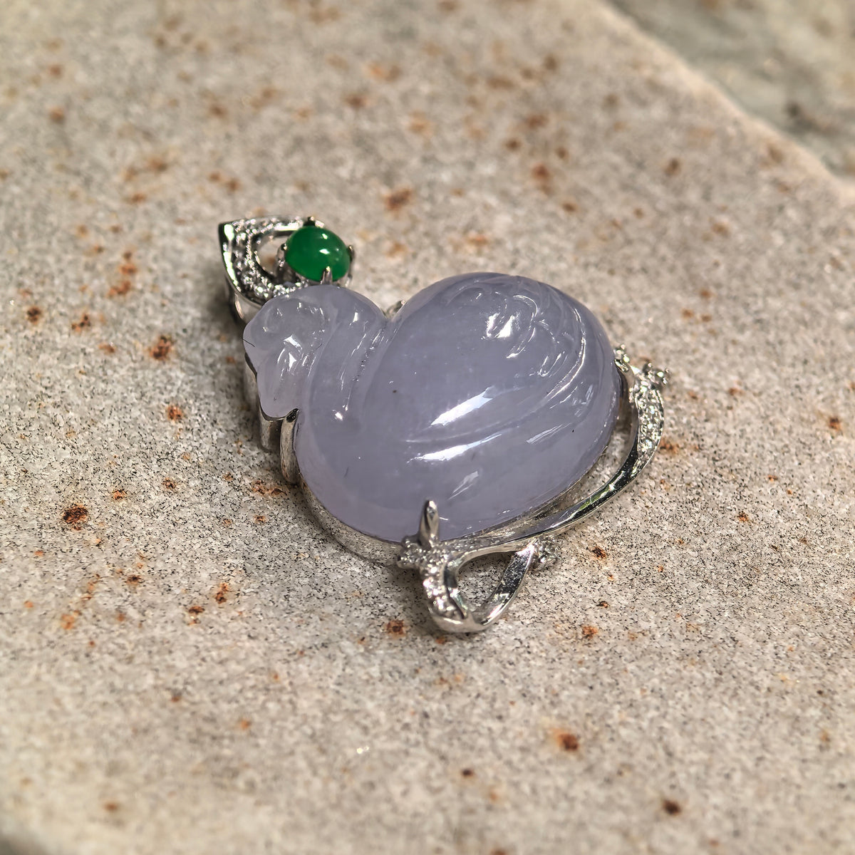 Angled close-up of a lavender jadeite swan pendant resting on stone, showing the rounded carving, prong setting and sweeping mount beneath the body.