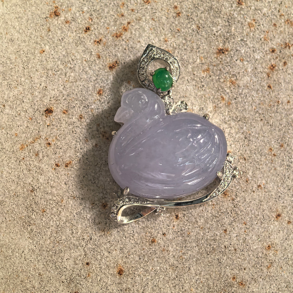 Front view of a lavender jadeite swan pendant on stone, highlighting the curved neck, carved wing and green accent beneath the pointed bail.