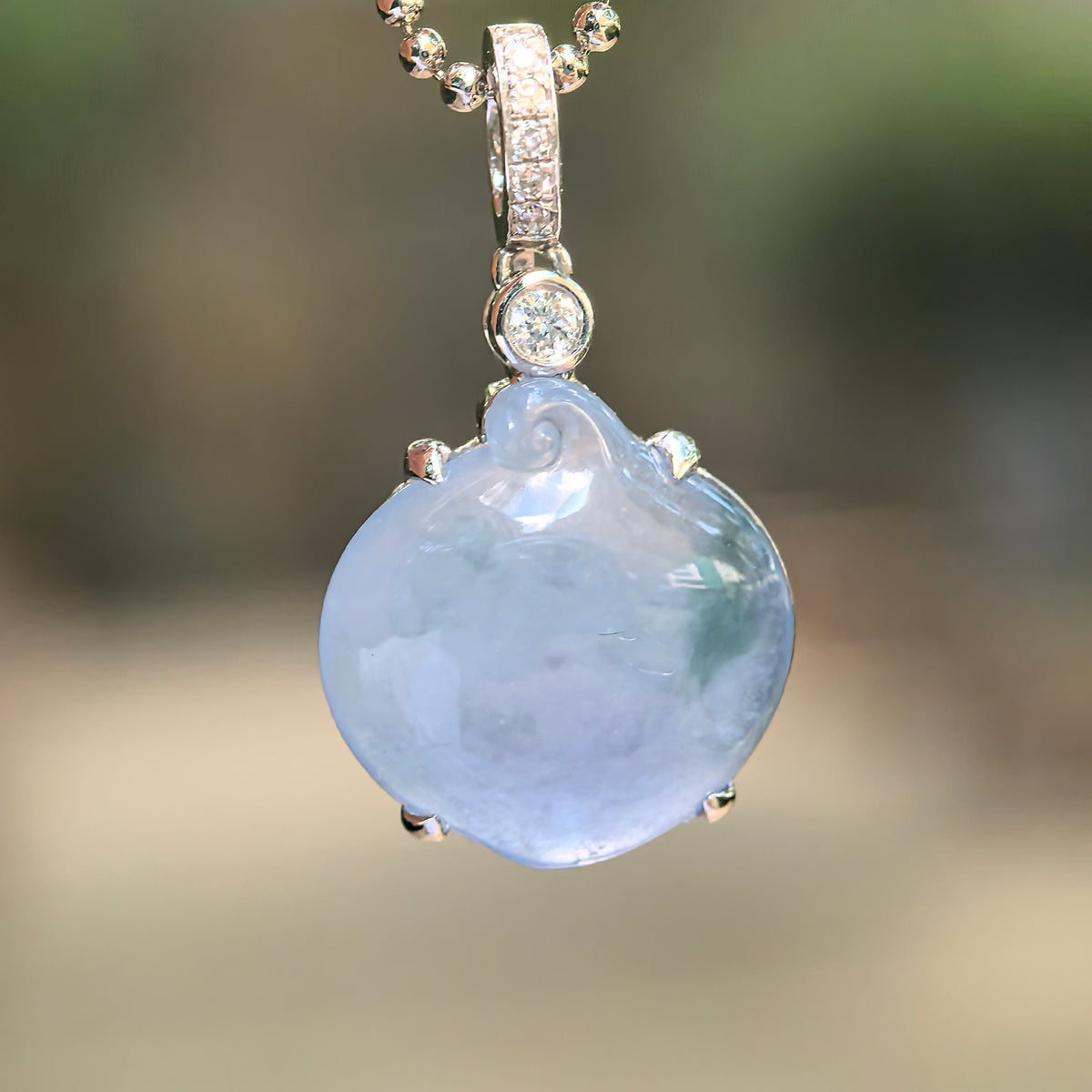 Lavender jadeite peach pendant suspended from a beaded chain, showing its green accent, curled top detail and diamond-set bail.
