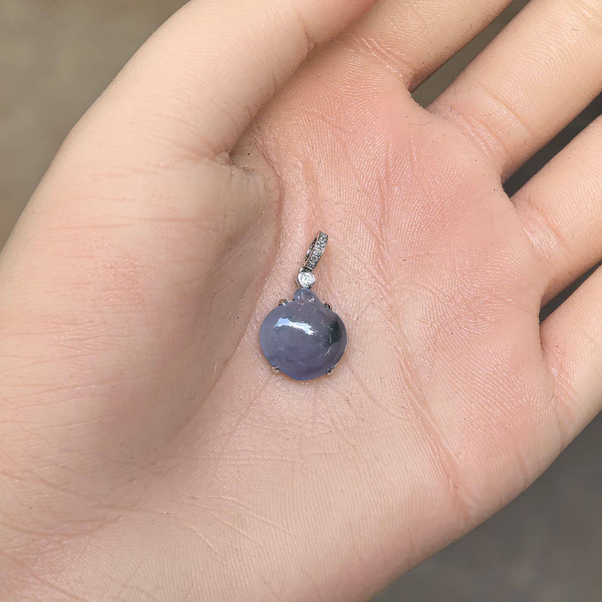 Lavender jadeite peach pendant displayed on an open palm, showing its petite proportions and 18K gold and diamond setting.