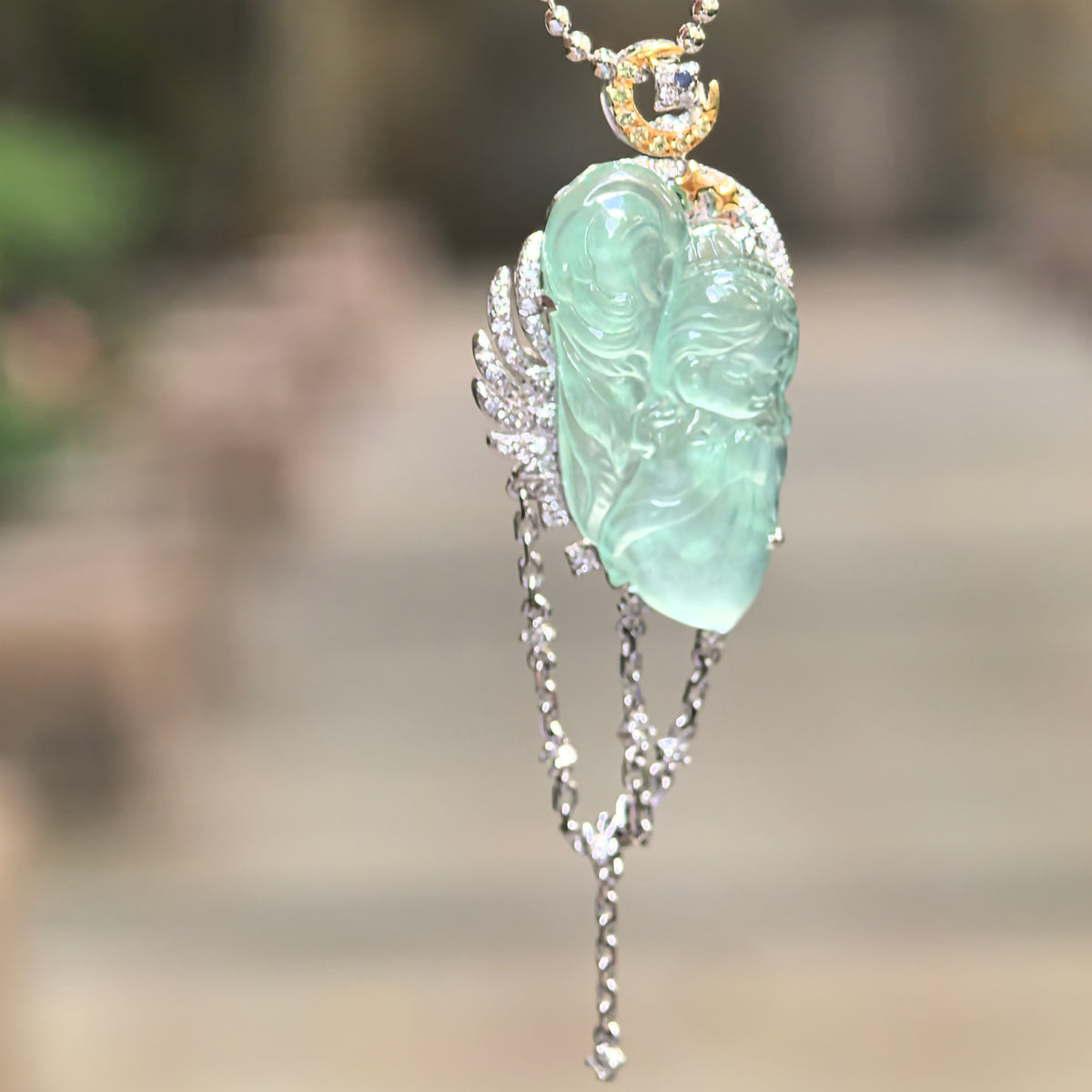 Soft green jadeite guardian angel pendant suspended from a beaded chain, showing the diamond-set wing, crescent-moon bail and draped chains.