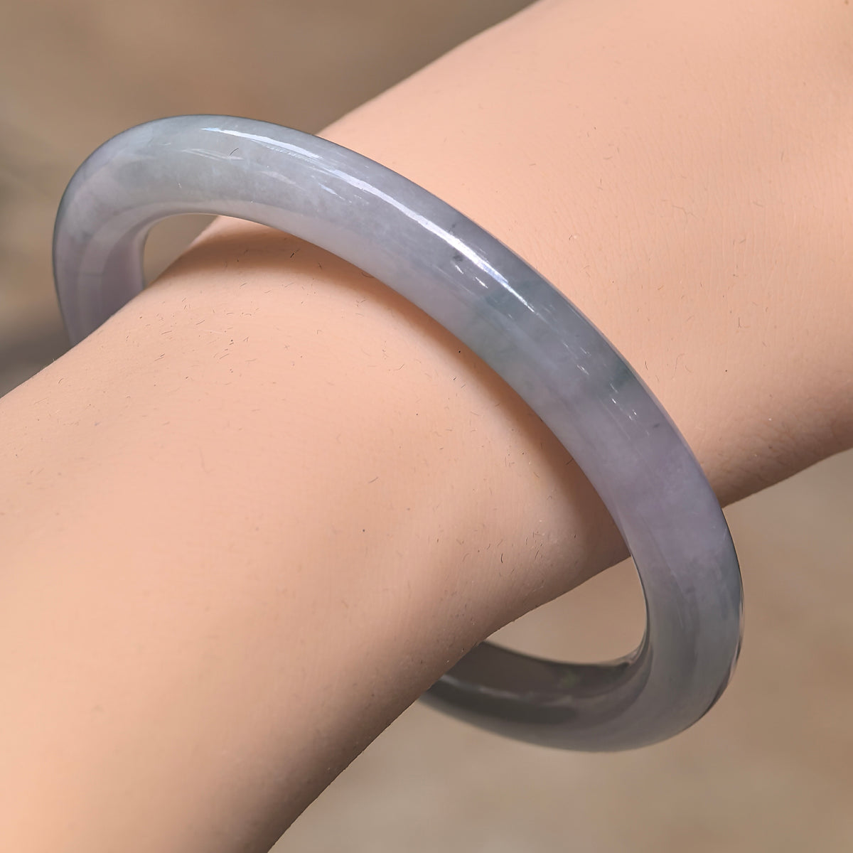 Angled wrist view of a pale lavender jadeite bangle with fine glutinous texture and a softly rounded profile.
