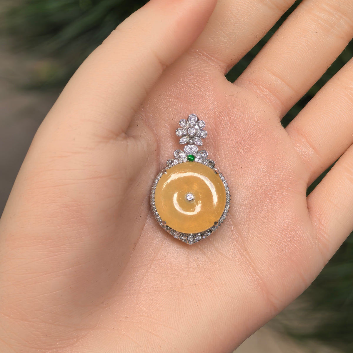 Yellow jadeite Peace Pendant displayed on an open palm, showing its circular center and ornate 18K gold and diamond setting.
