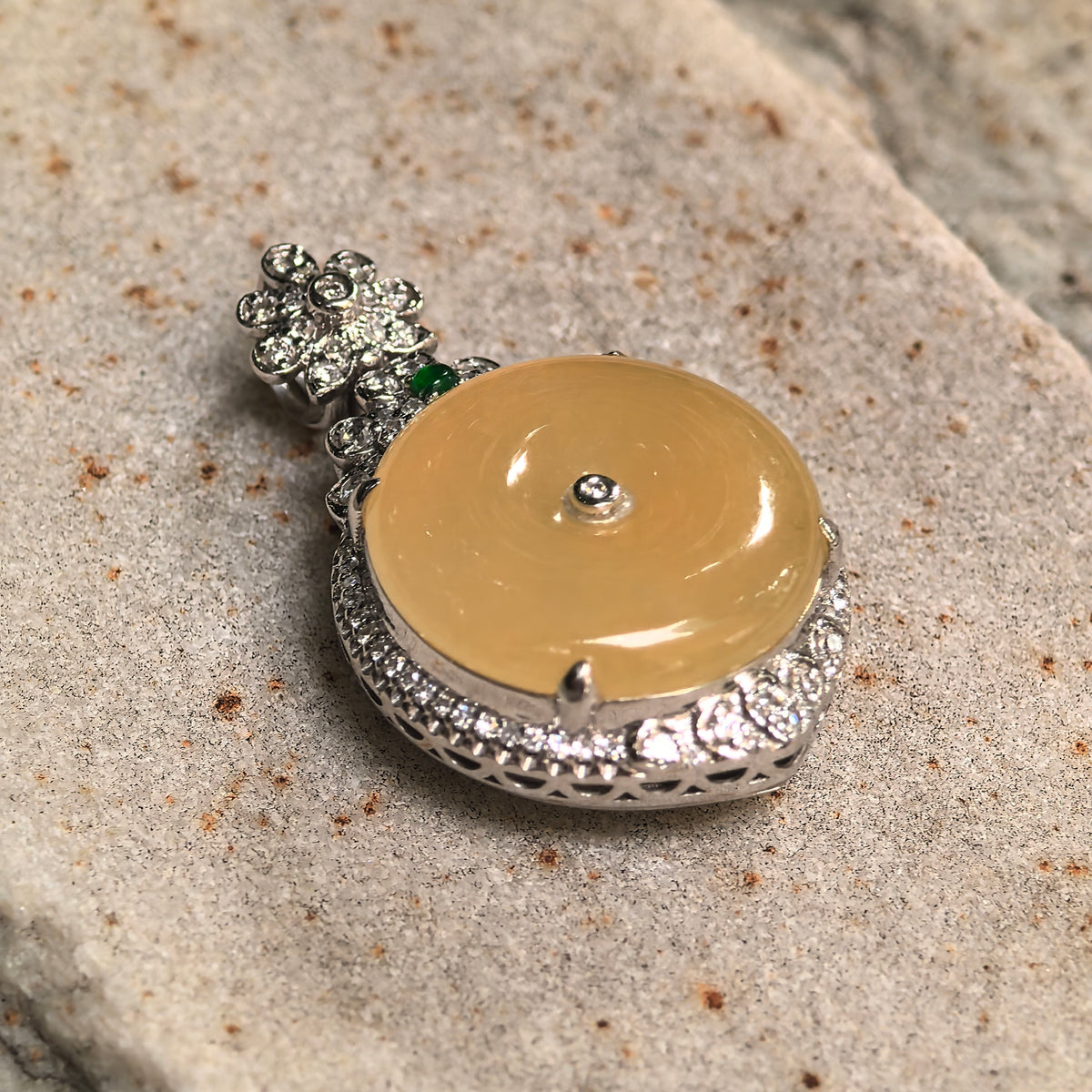 Angled view of a yellow jadeite Peace Pendant on stone, highlighting the domed jadeite, diamond border, and openwork sides of the setting.