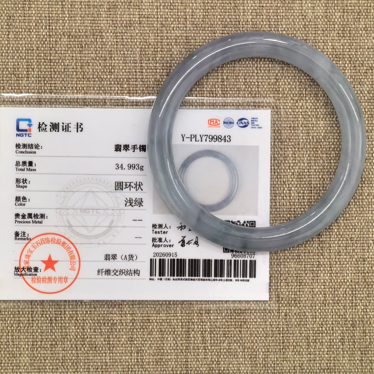 Pale lavender round-bar jadeite bangle displayed with its matching NGTC certificate on a woven background.