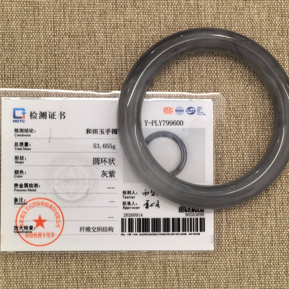 Smoky purple nephrite bangle displayed with its matching NGTC certificate on a tan woven background.