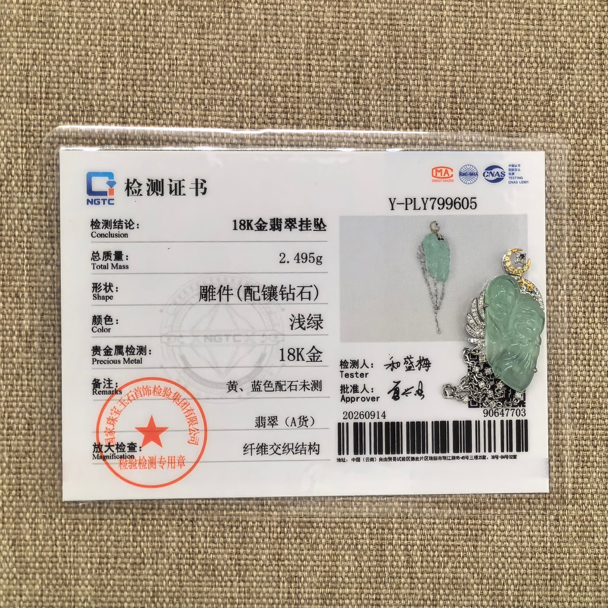 Green jadeite guardian angel pendant with an 18K gold and diamond setting displayed beside its matching NGTC certificate on a woven background.