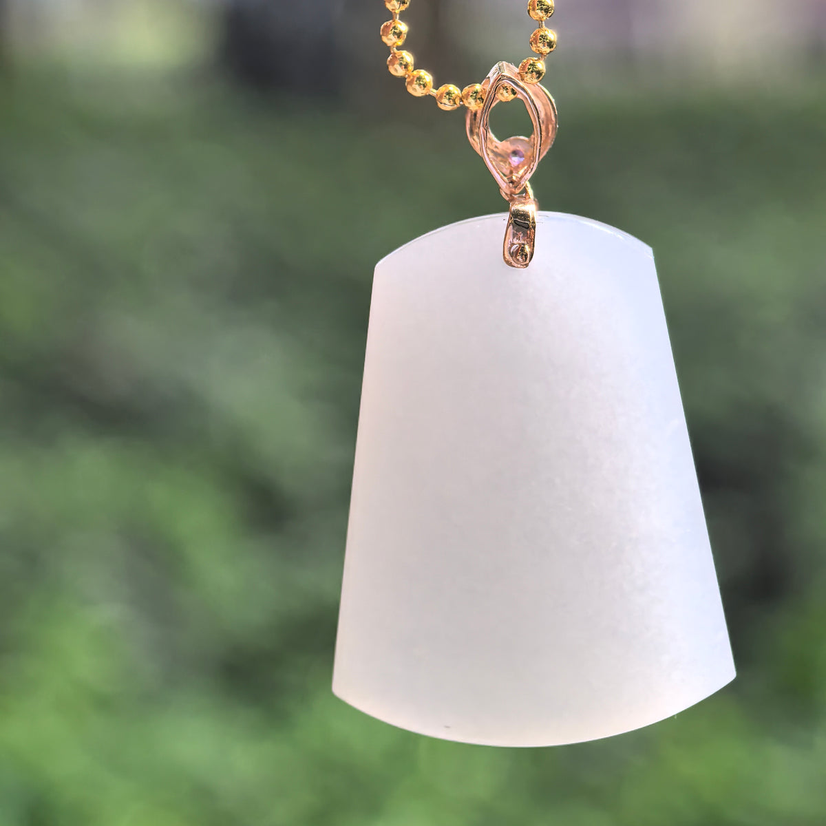White Hetian jade tapered plain plaque pendant hanging from a display chain, showing its curved lower edge and decorative 18K gold bail.