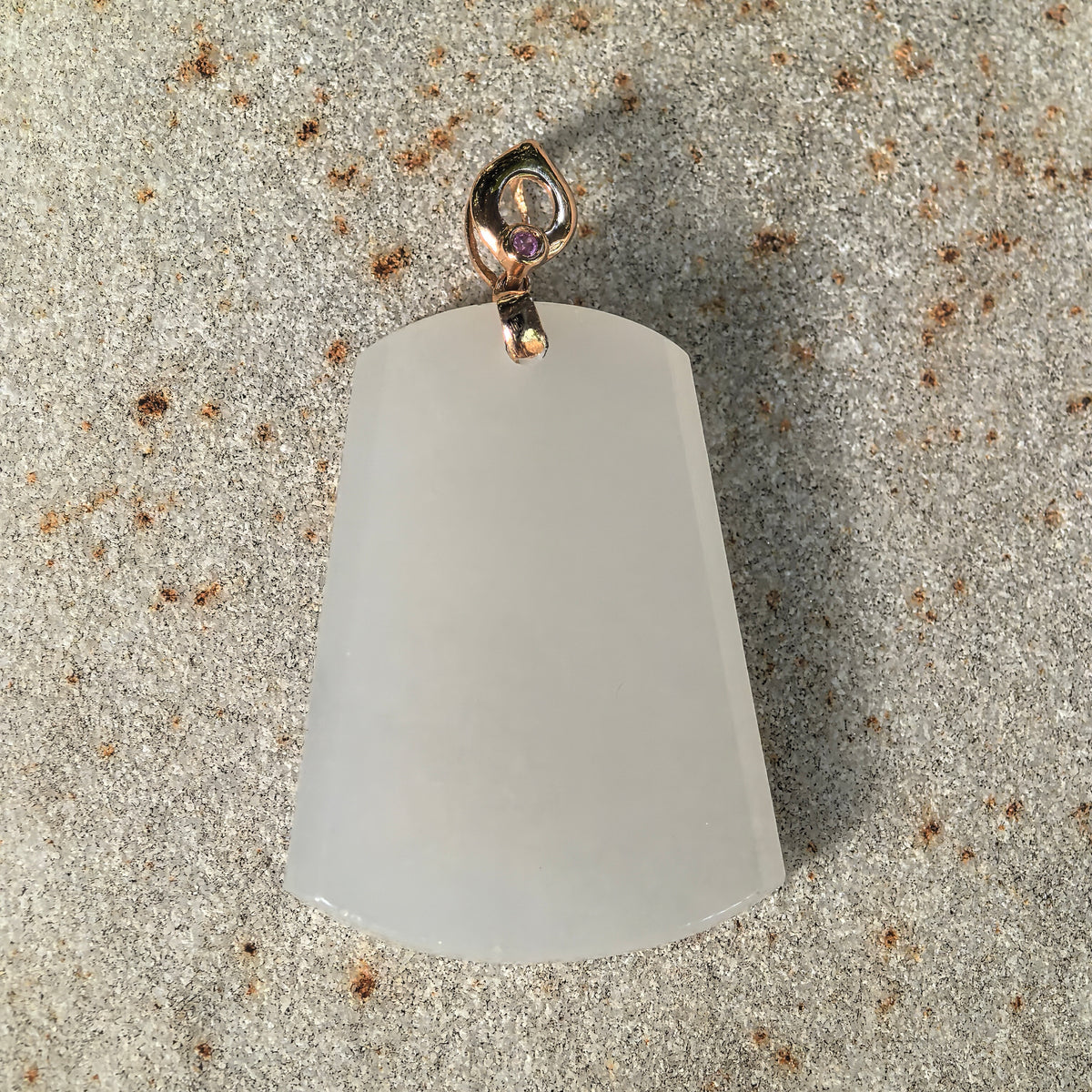 Front view of a white nephrite tapered plain plaque pendant on stone, showing its smooth face, curved edges and open 18K gold bail.