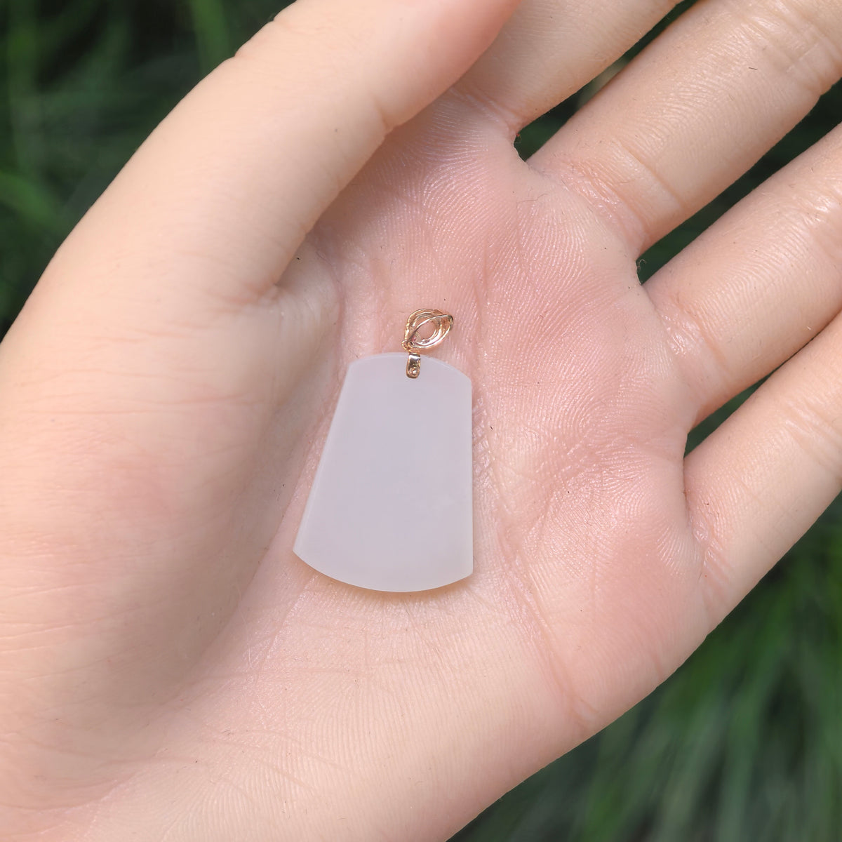 White nephrite plain plaque pendant resting on a palm, showing its tapered proportions, uncarved face and gold bail.
