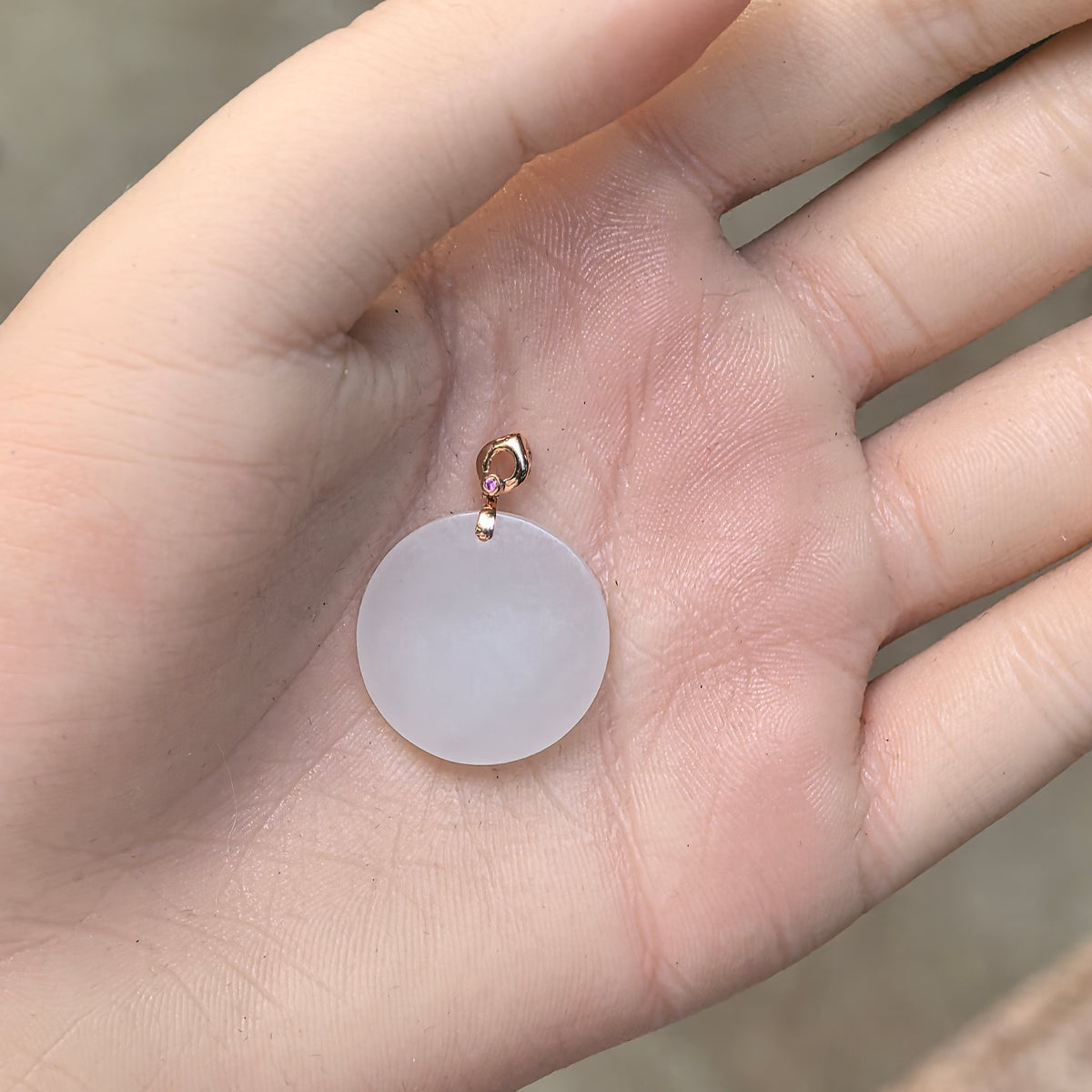 White Hetian jade round plain plaque pendant displayed on a palm, showing its proportions and decorative 18K gold bail.