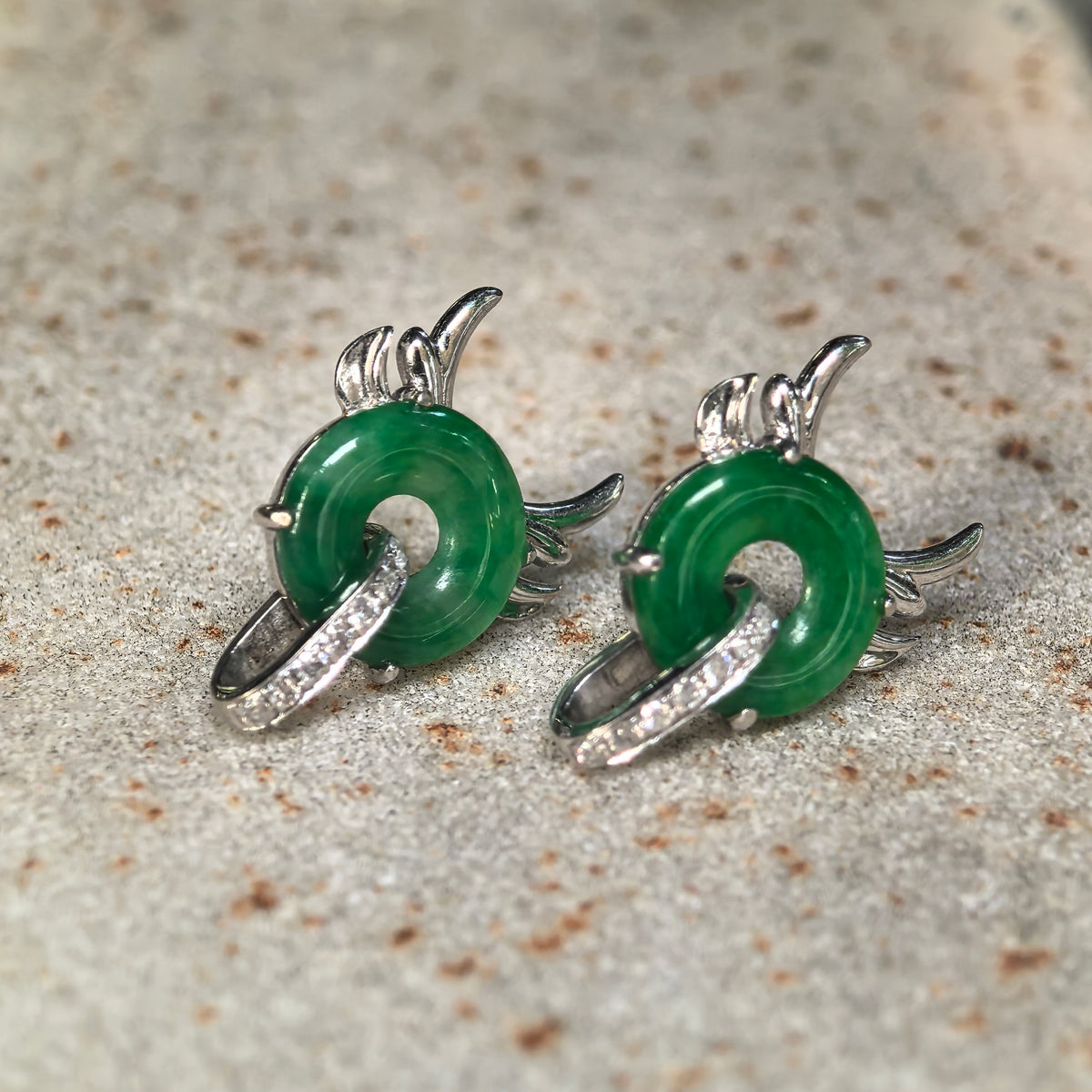 Angled view of green jadeite little devil earrings on stone, with polished jadeite discs and sculpted 18K gold details.