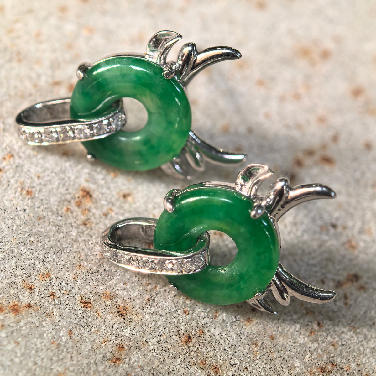 Close-up of green jadeite little devil earrings on stone, showing natural color variations and diamond-set loops passing through the jadeite centers.