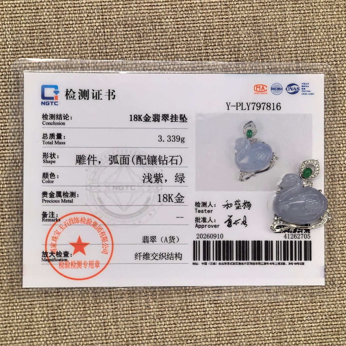 Lavender jadeite swan pendant in an 18K gold and diamond setting displayed beside its matching NGTC certificate on a woven background.