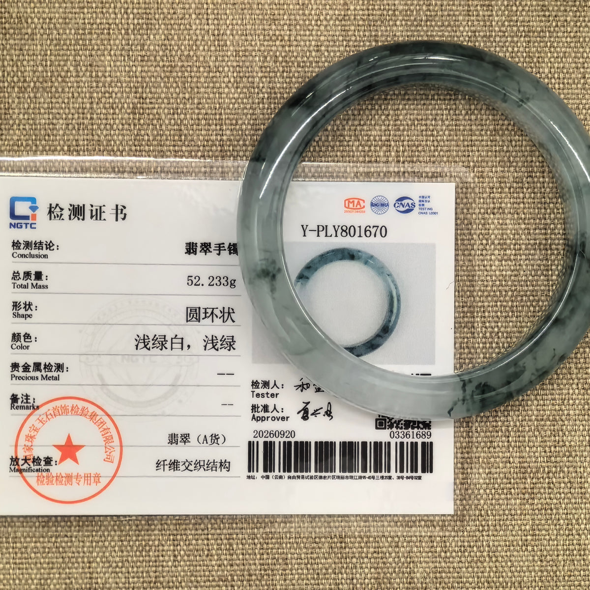 Dark green floating-pattern jadeite bangle displayed with its matching NGTC certificate on a woven background.