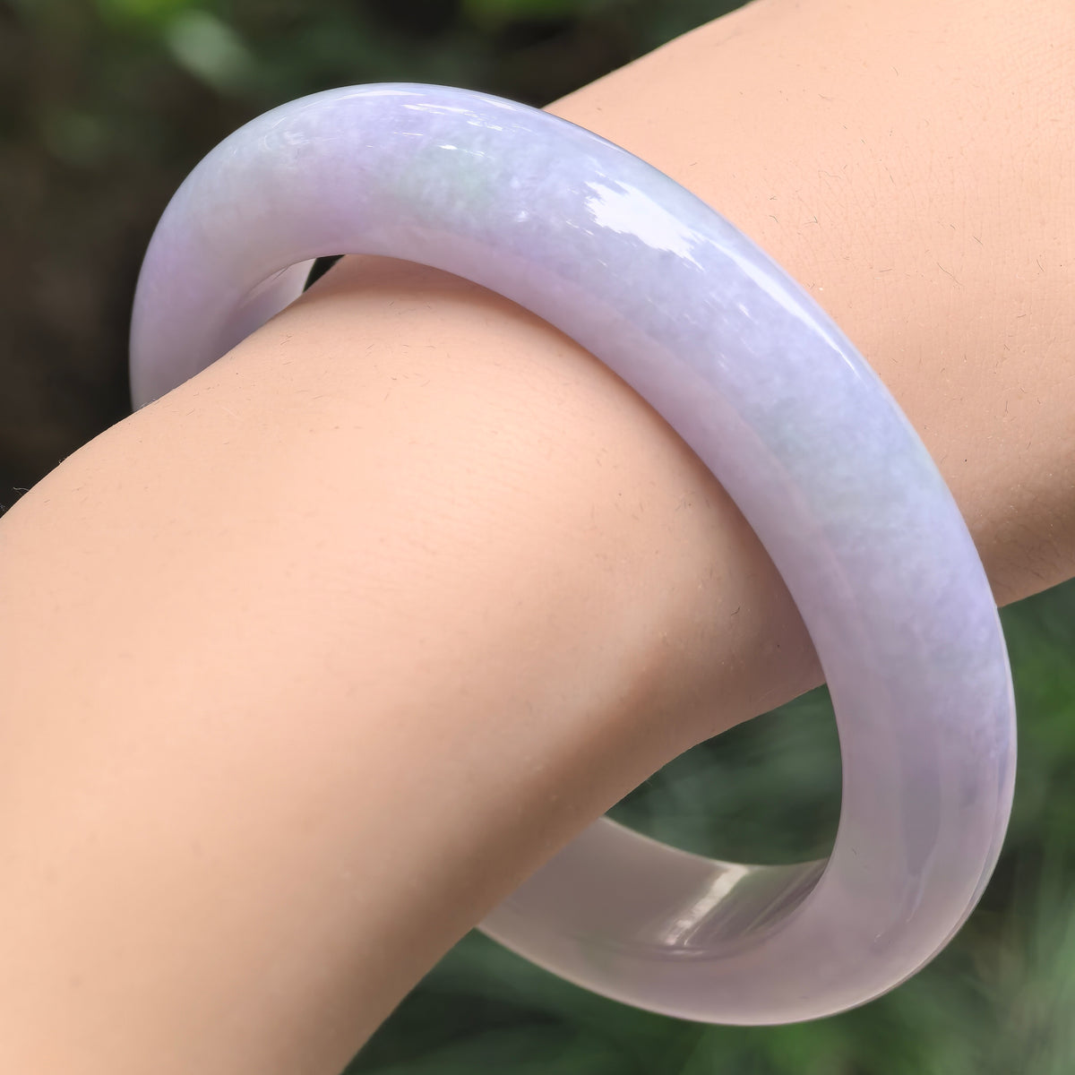 Angled wrist view of a pale lavender jadeite bangle, showing its thick profile, softly cloudy texture, and smooth inner face.